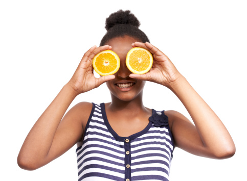Studio portrait of a happy young african american girl holding orange halves in front of her eyes isolated on white