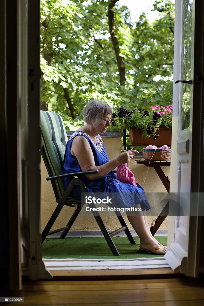 Senior mujer s'encuentra en el balcón y knits un pullover - Foto de stock de 70-79 años libre de derechos