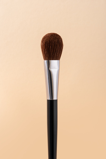 Makeup brush for applying face powder isolated on pastel beige background