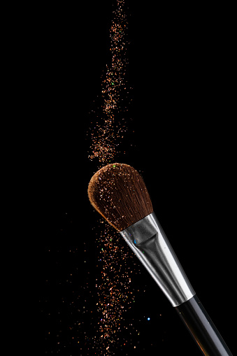 Golden glitter falls on make-up brush in black background. Luxury make-up concept.