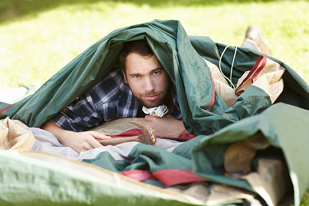 Frustrated young man struggling to erect a tent outdoors
