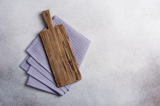 Old cutting board with linen napkin on grey concrete surface. Kitchen background with free space for text.