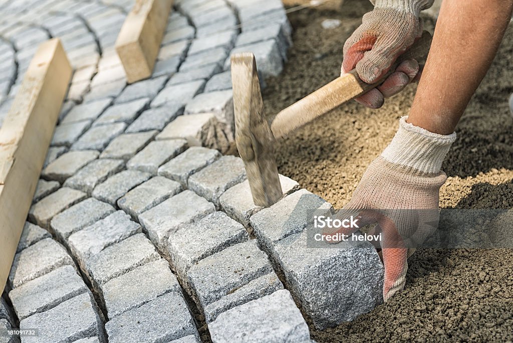 A workman's gloved hands use a hammer to place stone pavers Laying paving stone, just hands in gloves and a hammer in action, hammering on the paving stones. Paving Stone Stock Photo