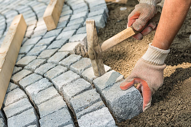 A workman's gloved hands use a hammer to place stone pavers stock photo