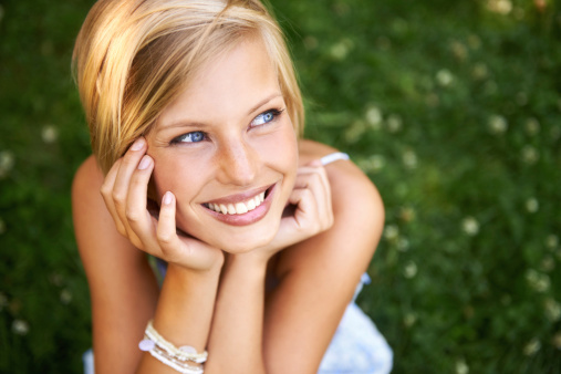 Attractive young blonde woman sitting and smiling on the grass outside