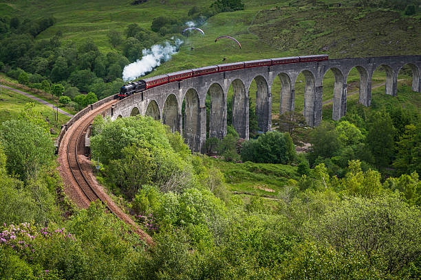Steam train crossing viaduct over Highland mountain glen Scotland White smoke puffing evocatively from a historic steam train thundering across the iconic arches of the Glenfinnan Viaduct over a green mountain glen deep in the Highlands of Scotland, UK. ProPhoto RGB profile for maximum color fidelity and gamut. lochaber stock pictures, royalty-free photos & images