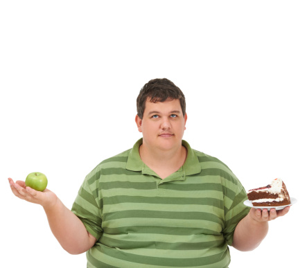 A obese young man holding an apple in one hand and a slice of cake in the other and looking up against a white background