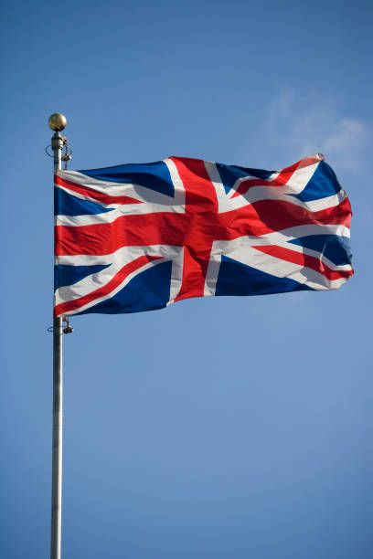 The British flag flying high on top of a flagpole British flag against a blue sky. Vertical.Copy space. union jack flag stock pictures, royalty-free photos & images