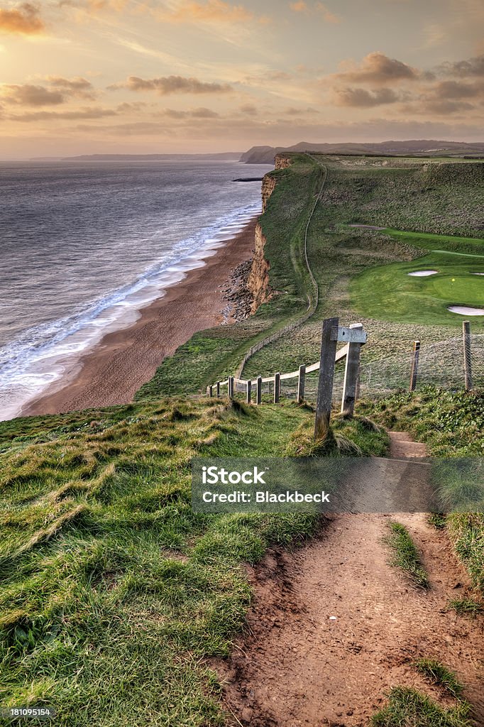 Footpath on the Dorset Jurassic Coast at sunset The South West Coast Path undulates westwards towards West Bay on the Dorset Jurassic Coast. The cliff .in the middle distance is Golden Cap, the highest sea cliff on the south coast of England. Beach Stock Photo