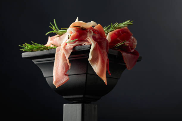 Prosciutto with rosemary on a black podium.