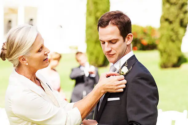 Side view of mother pinning boutonniere on groom's suit at garden wedding. Horizontal shot.