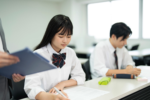 Asian teenagers in high school uniforms doing test in class
