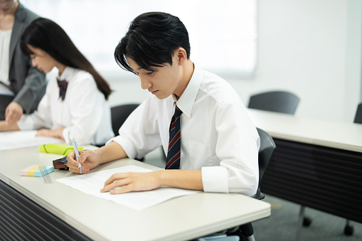 Asian teenagers in high school uniforms doing test in class