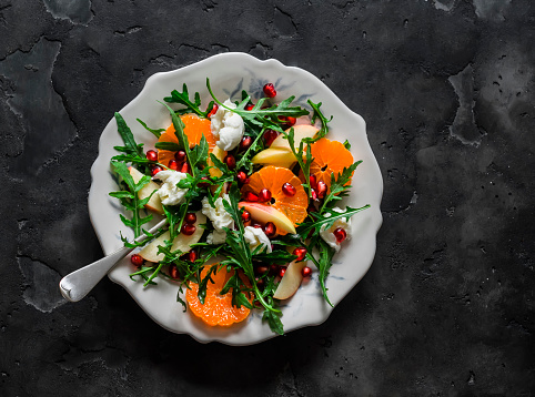 Rocket salad with tangerines, pomegranate, apples and mozzarella cheese on a dark background, top view