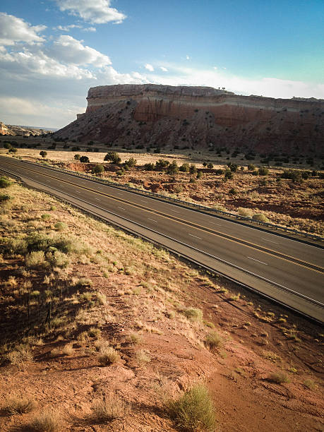 mobilestock southwest road trip a four lane highway cuts through the desert badlands landscape underneath a cloud filled moody sky.  such beautiful nature scenery and travel experience can be found on zia pueblo in new mexico.  mobilestock vertical wide angle and high angle composition with vignette and retro color treatment. sonoran desert desert badlands mesa stock pictures, royalty-free photos & images