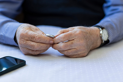 Hands of 87 years old adult senior preparing hearing aid for use at home kitchen.