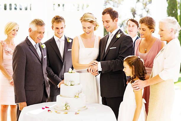 Guests Looking At Bride And Groom Cutting Cake During Reception