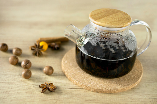 Fragrant black tea is brewed in a glass teapot on a wooden background decorated with nuts and spices. Concept of Christmas and New Year.