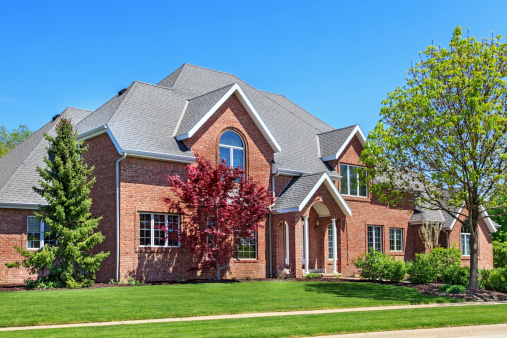 Beautiful two story red brick home nicely landscaped with blue sky in the background.