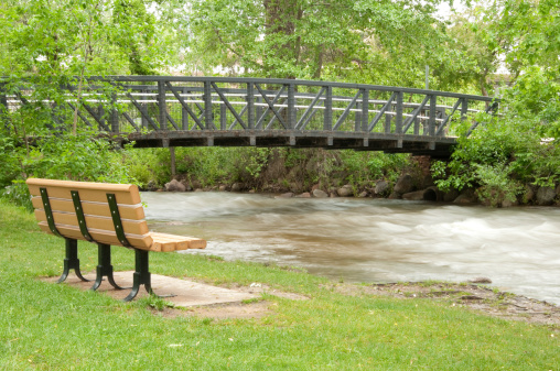Boulder creek bridge in downtown boulder colorado with a bench in the foreground. .