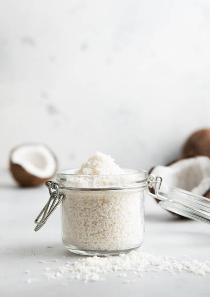 istock Shredded sweet coconut flakes in glass jar with ripe coconuts on light table.Macro 1811090141