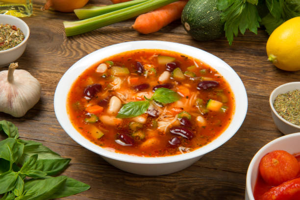 Italian minestrone soup in a white porcelain soup bowl on a rustic wooden table with ingredients. stock photo