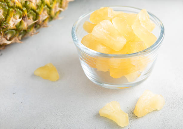 istock Dried soft sweet pineapple slices in glass bowl with raw pineapple on light table. 1811097545