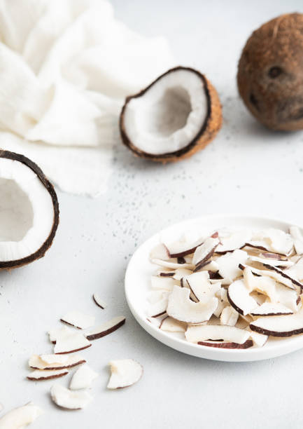 istock Plate with dried organic coconut slices chips and whole ripe coconut on light background.Macro. 1811097546