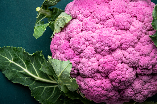 Fresh organic purple cauliflower cabbage with leaves on old rustic green table background, top view