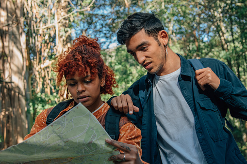 travel multi-ethnic young couple with map and backpacks in nature