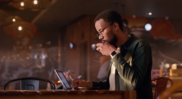 Black man, tablet and drinking coffee at restaurant for research, internet or connection at indoor cafe. African male person with technology having a cappuccino, espresso or latte at diner or shop