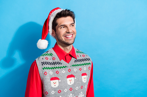 Photo portrait of handsome young guy beaming smile look empty space wear x-mas print vest hat outfit isolated on blue color background.
