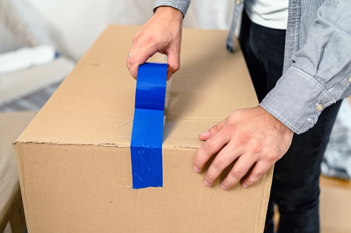 A man uses adhesive tape to packing cardboard box. Moving home concept