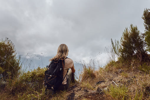 Rear view of carefree female backpacker relaxing on a mountain and looking at view. Copy space.