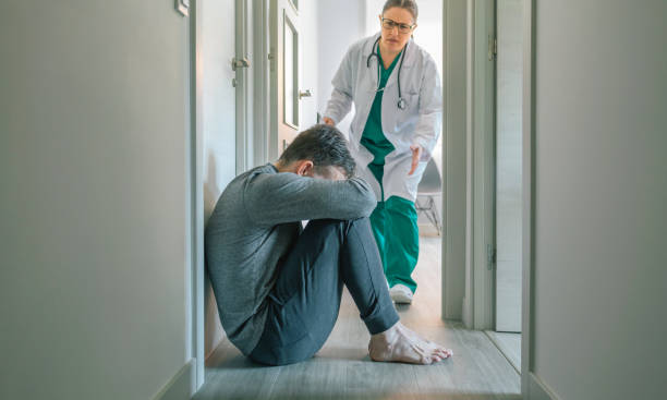 Female doctor running to help patient with mental disorder sitting on floor stock photo