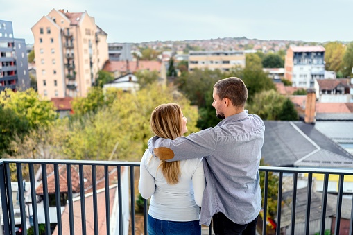 Couple standing on their new apartment terrace and enjoying in beautiful view. Real estate and moving theme.