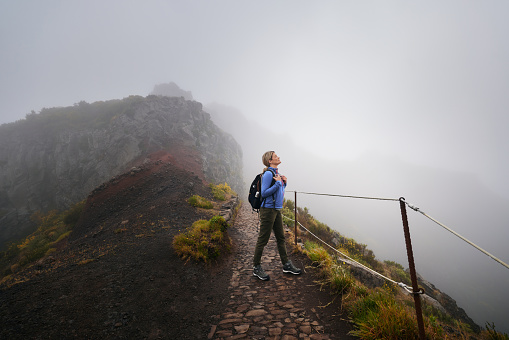 Smiling female backpacker inhaling the fresh air during foggy day on a mountain. Copy space.