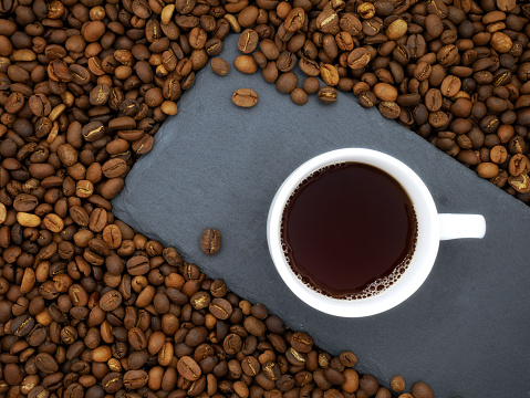 Coffee cup on stone slab on coffee beans texture background.Top view.