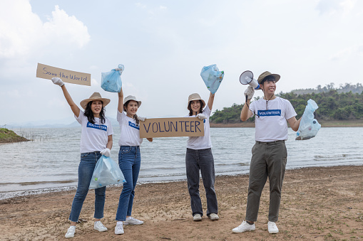 Group of volunteers holding rubbish bags and sign to campaign to save the global environment. clean up garbage in tourist attractions. Conservation and care cleanliness in nature.