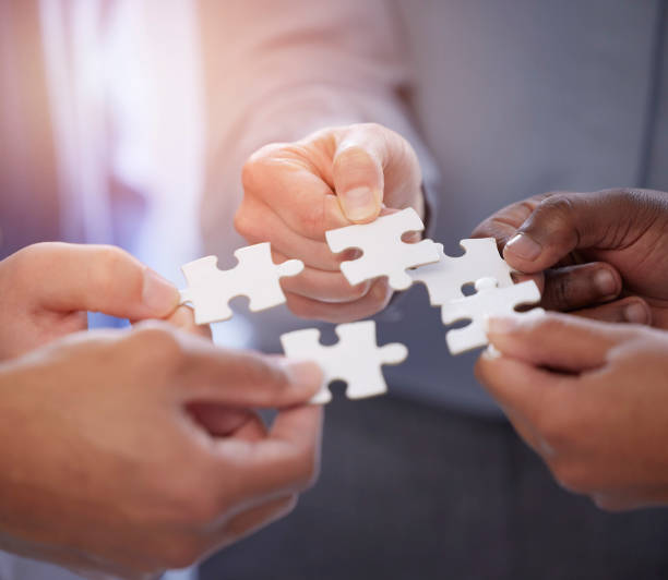 istock Business people, hands and teamwork with puzzle collaboration for problem solving, growth and development. Meeting, diversity and coworking jigsaw in team building huddle, men and women with solution 1811194491