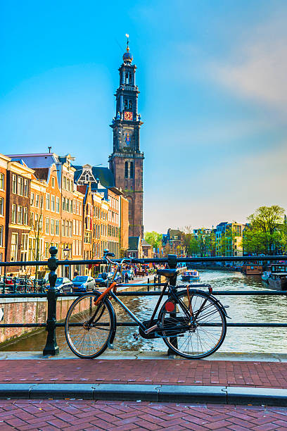 Typical Amsterdam City Scene. Visible are one of the many beautiful bridges, one bike, traditional dutch houses and tower of Westerchurch in the background. Amsterdam, Netherlands.
