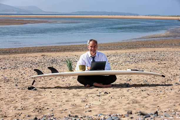 istock Mature businessman laptop on beach and surfboard 181120555