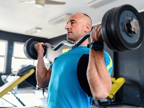 Confident man training muscles with a barbell in the gym