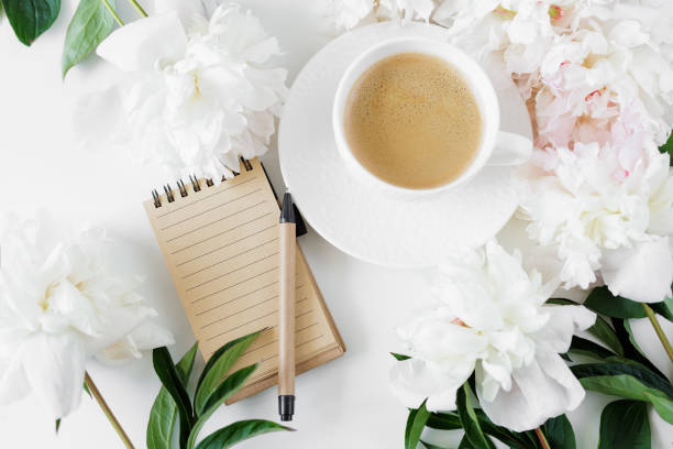 Top view of coffee cup, notebook, pen and pionies on table