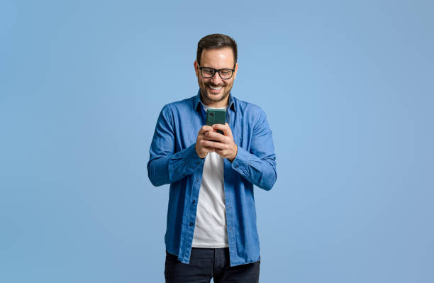 istock Male freelancer smiling and using social media over smart phone while standing on blue background 1811249921