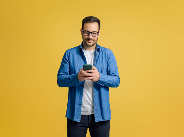 istock Confident serious businessman checking messages over mobile phone isolated on yellow background 1811250457