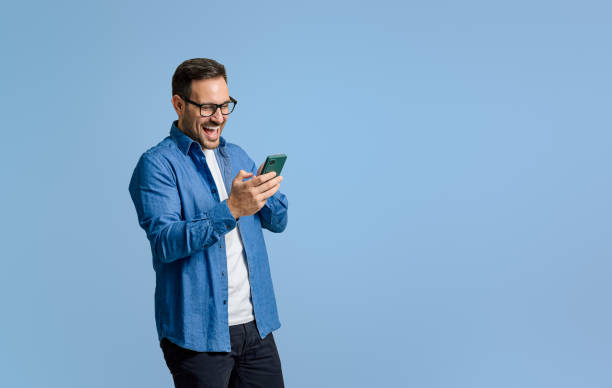 istock Young businessman laughing ecstatically while reading messages over mobile phone on blue background 1811250461