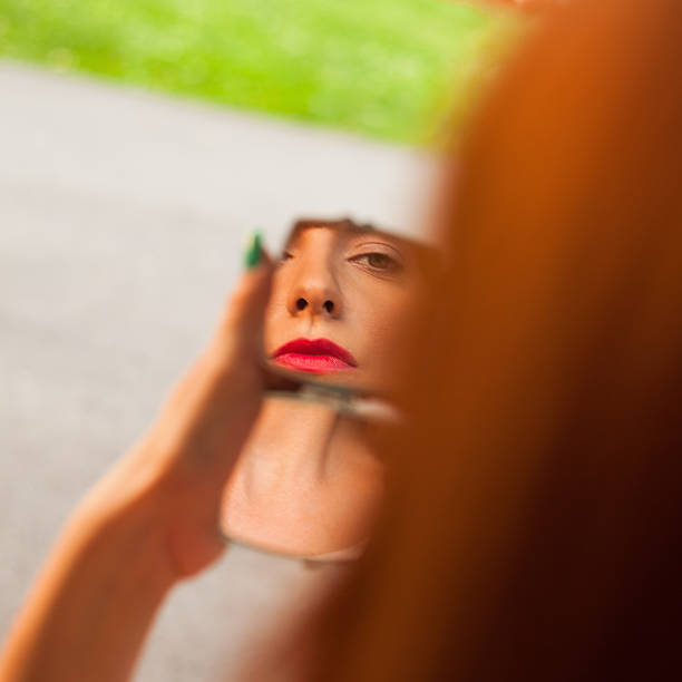 Beautiful young woman applying lipstick outdoors.