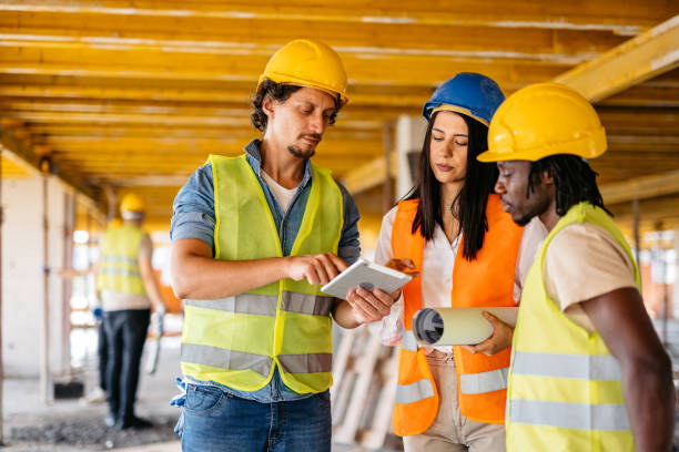 istock Female Engineer Showing The Blueprint On A Tablet To The Construction Workers On A Construction Site 1811260513