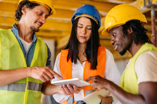 istock Female Engineer Showing The Blueprint On A Tablet To The Construction Workers On A Construction Site 1811268792